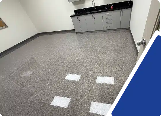 An empty room with light speckled flooring and grey cabinets under a dark countertop.