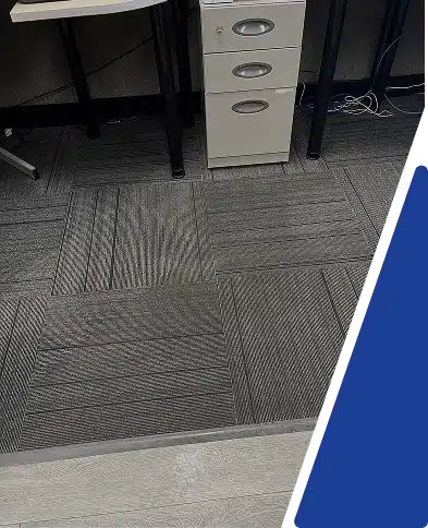 A close-up view of patterned gray carpet tiles under an office desk.