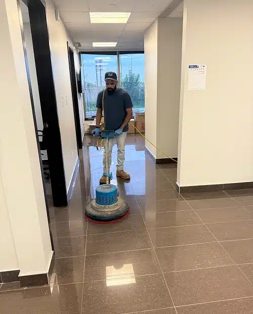 A cleaner mopping a brightly lit office hallway.