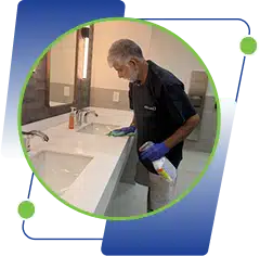 A man wearing blue gloves cleaning a white bathroom sink.