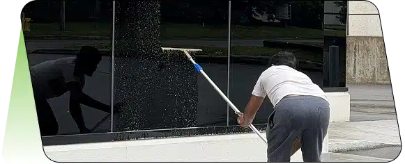 Close-up of an extension pole squeegee cleaning soapy, dark exterior glass.