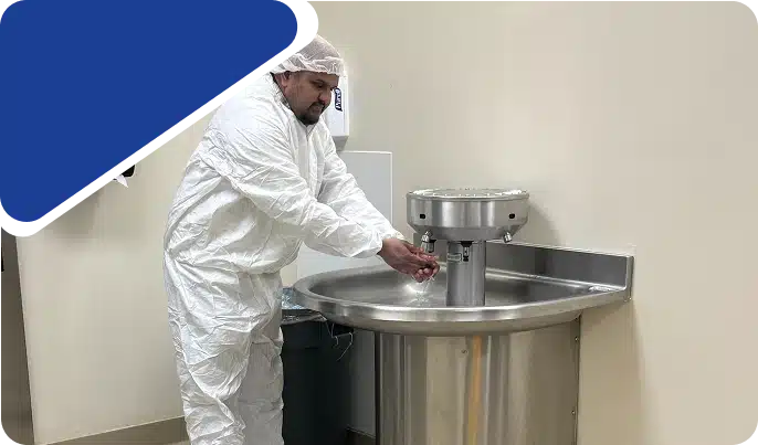 A worker in a white protective suit using a large stainless steel industrial sink, framed by a blue graphic.