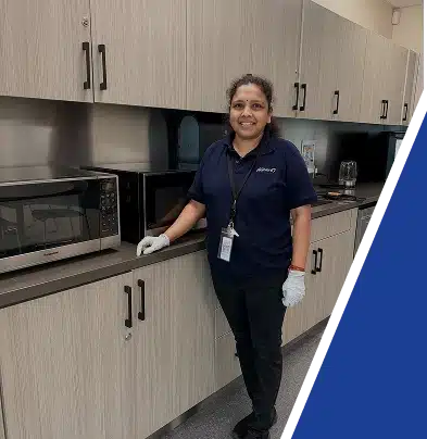 A smiling day porter in a dark blue uniform standing in an office breakroom.