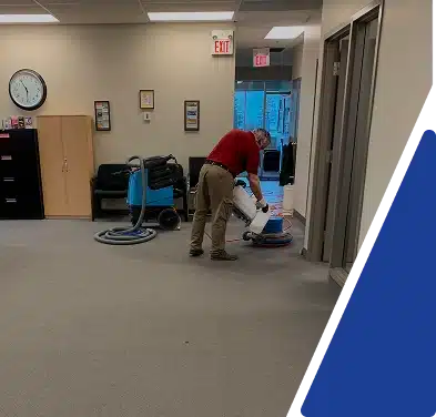 A person vacuuming the carpet in an office setting, framed by blue and white graphics.