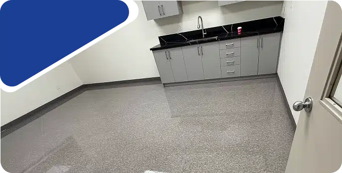 An empty room featuring light-colored flooring and grey cabinets with a dark countertop, framed by a blue graphic.