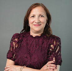 Headshot of a smiling woman wearing a dark red patterned blouse.