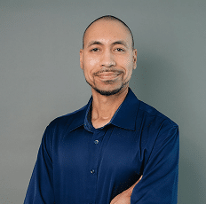 Headshot of a smiling man with a goatee wearing a dark blue collared shirt.