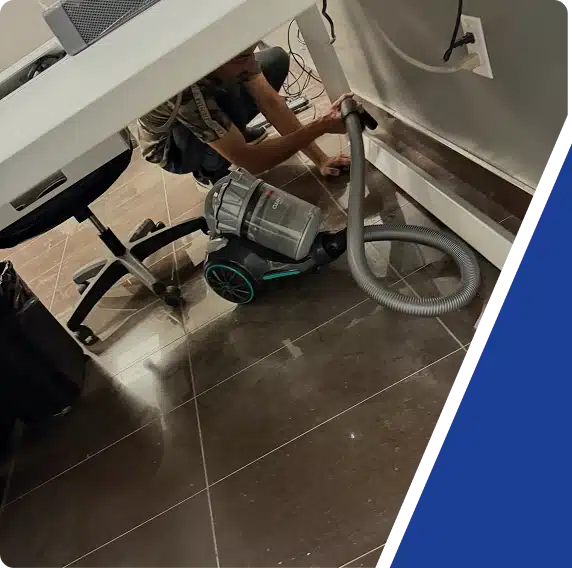 A person vacuuming the carpet under an office desk, framed by a blue graphic.