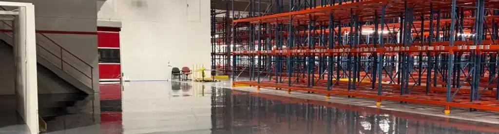 An empty warehouse interior with polished floors and red metal shelving units.