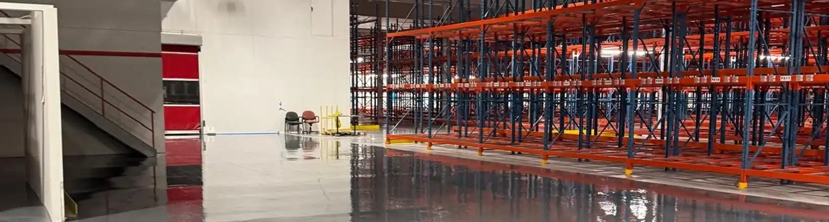 An empty warehouse interior with polished floors and red metal shelving units.