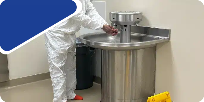 A worker in white protective clothing at a large stainless steel industrial sink or vat.