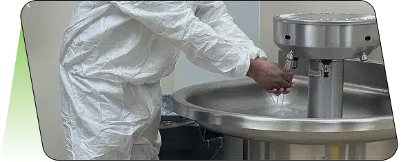A close-up of a worker in a white protective suit washing their hands in a stainless steel sink.