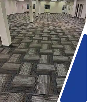 A large empty room featuring patterned gray carpet tiles and white columns.