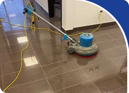 A blue floor buffing machine resting on a shiny brown tiled hallway floor, framed by a blue graphic.
