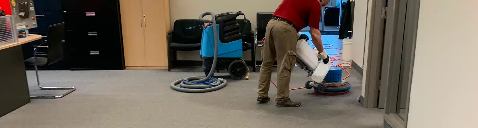 A worker operating a carpet cleaning machine in an office setting.