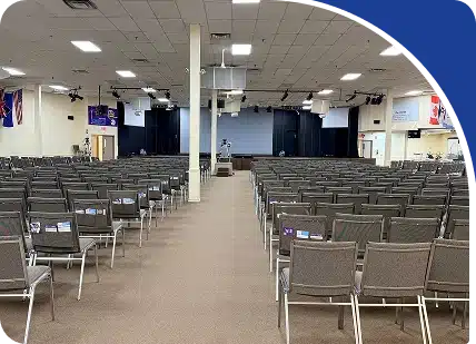 A large auditorium or place of worship with many rows of chairs facing a stage area, framed by a blue graphic.