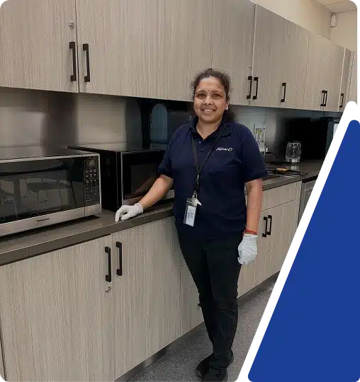 A smiling day porter in a dark blue uniform standing in an office breakroom, framed by a blue graphic.