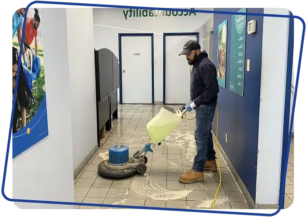 A cleaner in a dark uniform mopping a tiled hallway floor next to a yellow mop bucket.