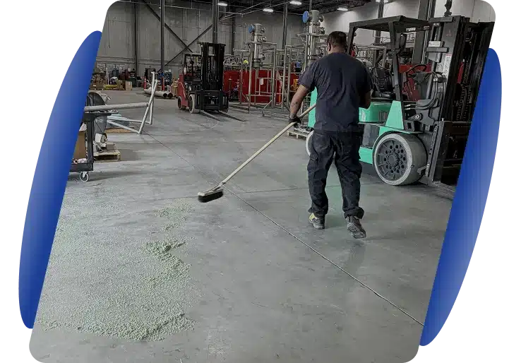 A worker sweeping a concrete floor in a large industrial warehouse or factory setting.